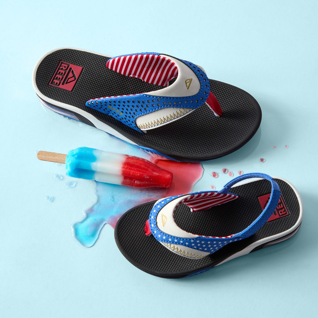 Kids Fanning right-facing sandal close-up and left-facing back strap shown with melted red, white, and blue popsicle on blue background